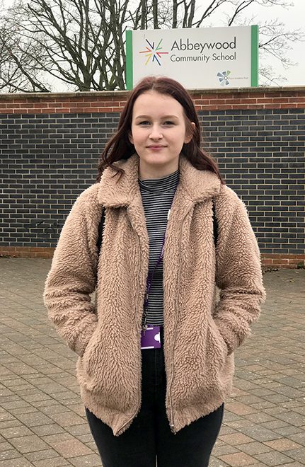 Photo of Lauren Brenton, standing in front of a sign for Abbeywood Community School.