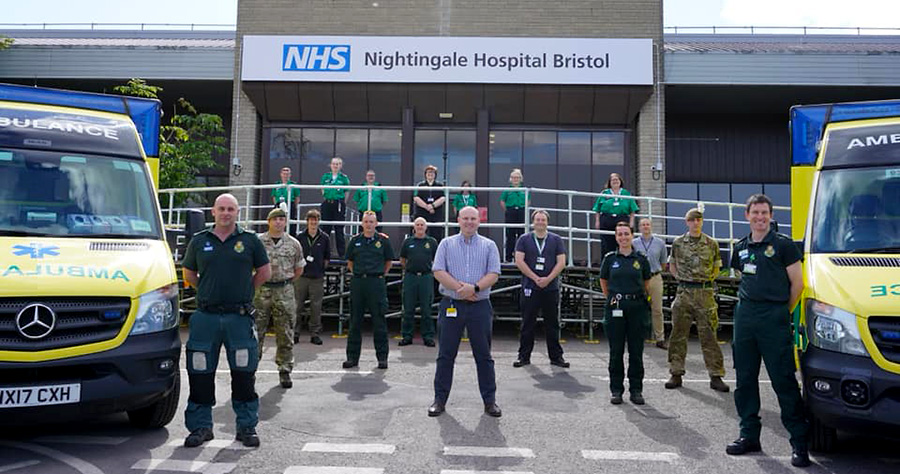 Photo of paramedics, ambulance teams, army personnel and hospital staff standing in front of NHS Nightingale Hospital Bristol.