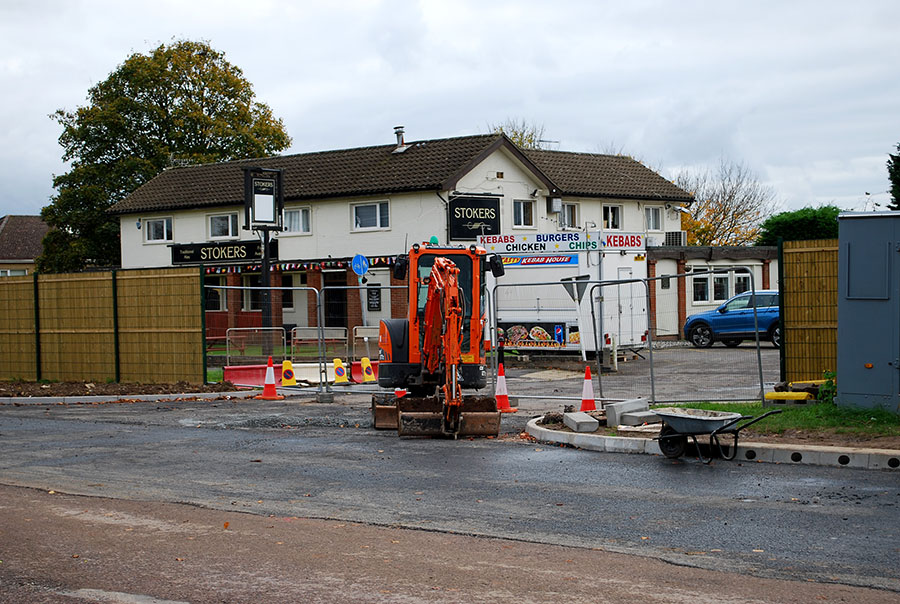 Photo of a mini-excavator being used for highway works, with a public house in the background.