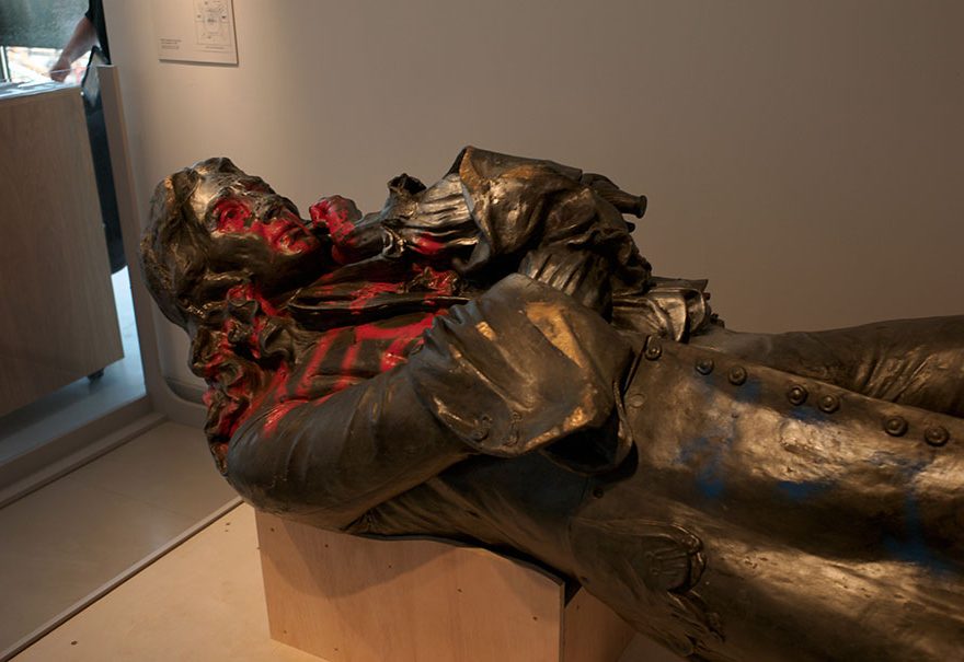 Photo of a statue lying horizontal and daubed in red paint.