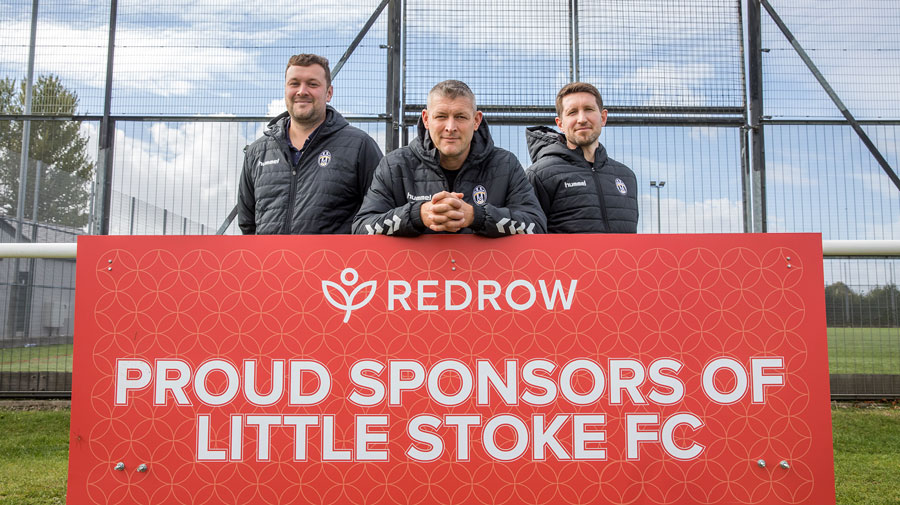 photo of three football players standing behind an advertising board.