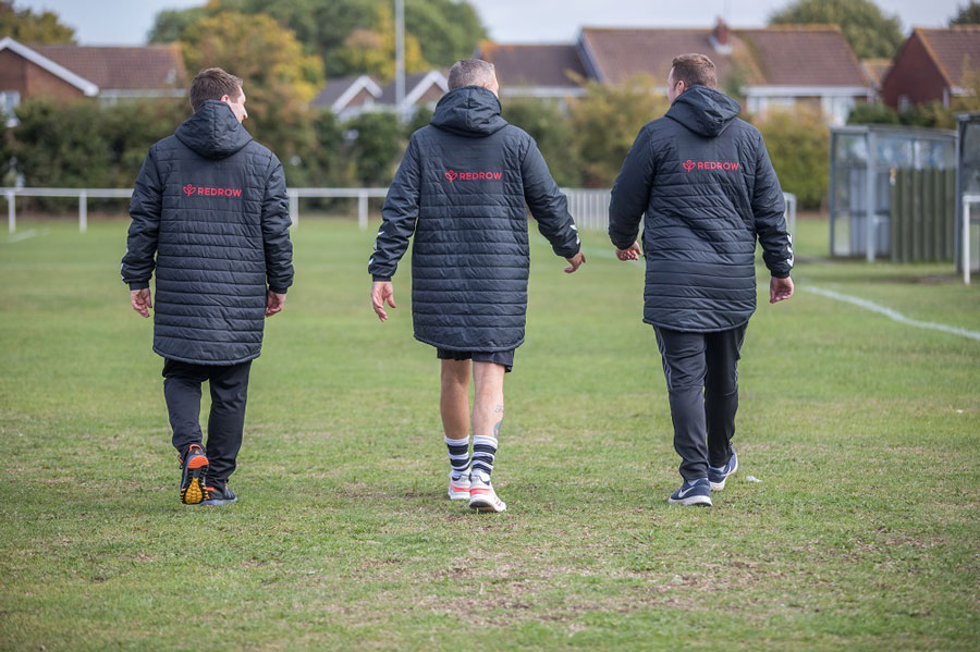 Photo of three football players wearing coats walking away from the camera.