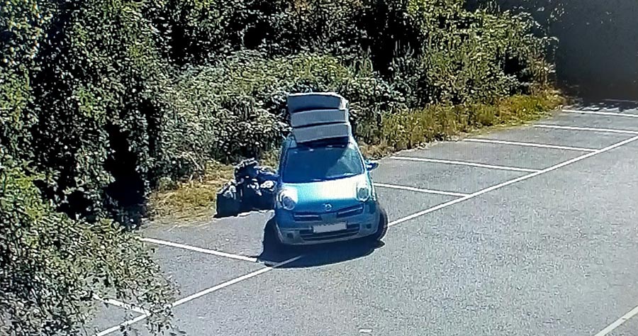 Photo of a car with mattresses on a roof rack and a number of black bin backs on the ground alongside it.