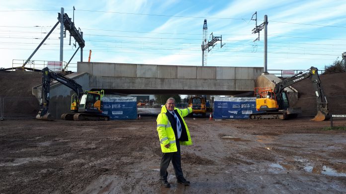 Photo of a person in a hi-vis jacket standing in front of a railway bridge.