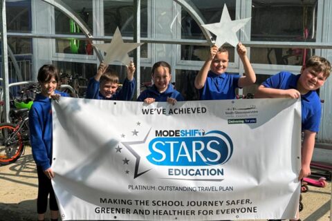 Photo of a group of school children holding silver star shapes and a banner.