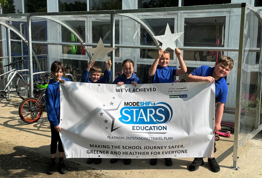 Photo of a group of school children holding silver star shapes and a banner.