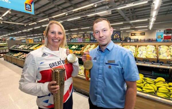 Photo of a two people in a supermarket, one wearing a track suit and holding a medal.