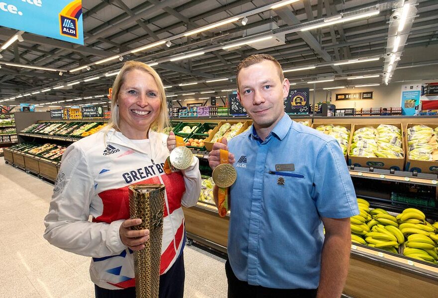 Photo of a two people in a supermarket, one wearing a track suit and holding a medal.