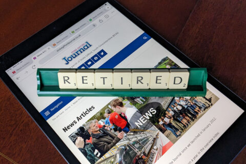 Photo of letter tiles spelling the word 'Retired' in a rack placed over a webpage displayed on an iPad.