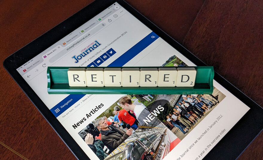 Photo of letter tiles spelling the word 'Retired' in a rack placed over a webpage displayed on an iPad.