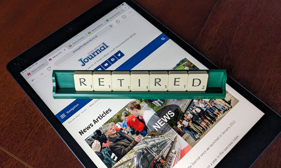 Photo of letter tiles spelling the word 'Retired' in a rack placed over a webpage displayed on an iPad.